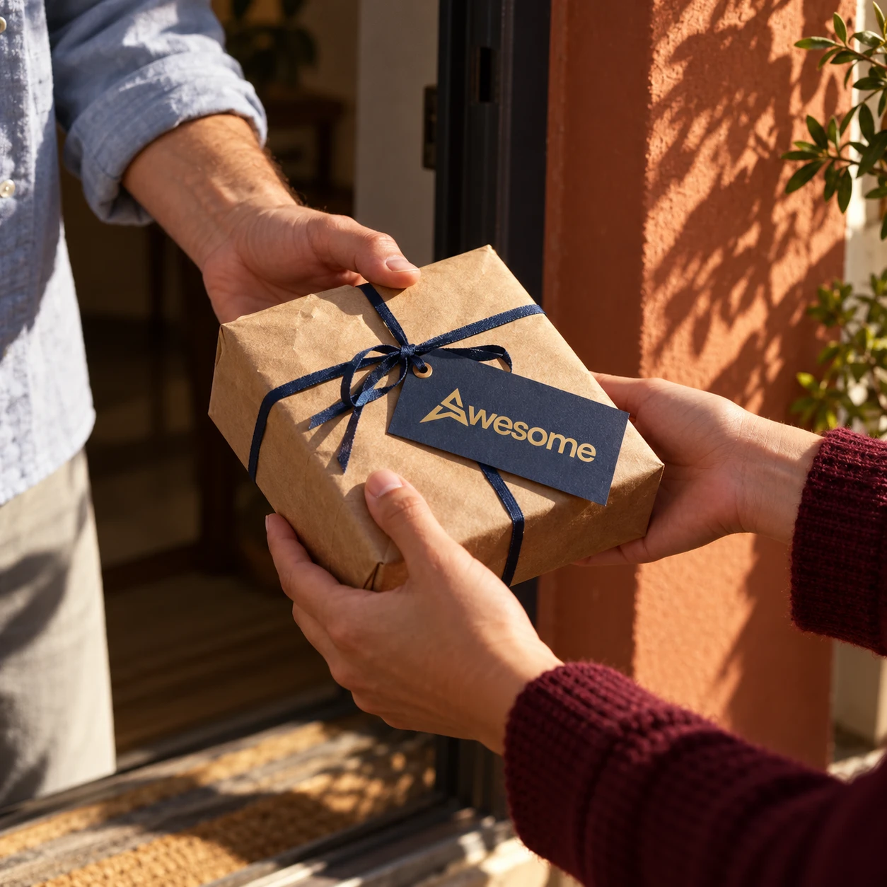 Hands passing a kraft-wrapped gift tied with navy ribbon and an Awesome tag at a sunlit doorway