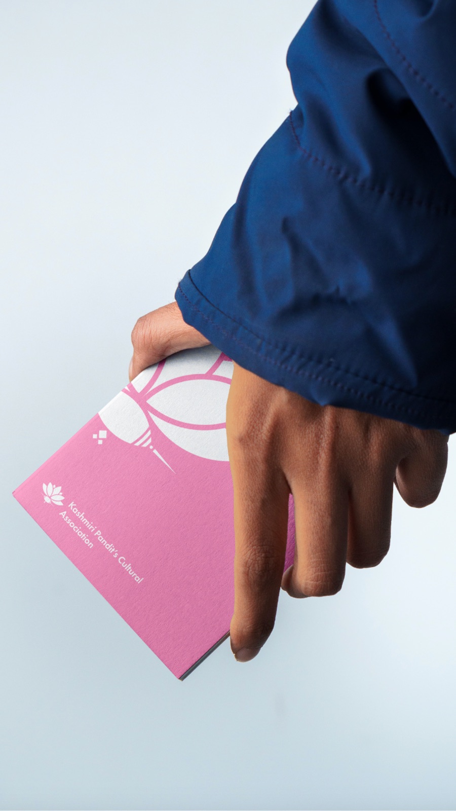 A hand holding a deep pink KPCA booklet with the white lotus mark